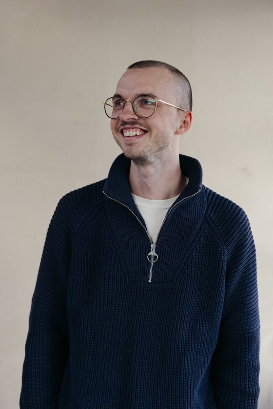 Johannes smiling and looking to the side, wearing round glasses and a navy knit sweater.